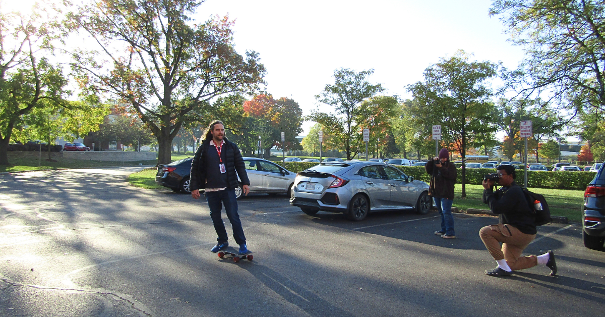 man on skakeboard being photographed by two students